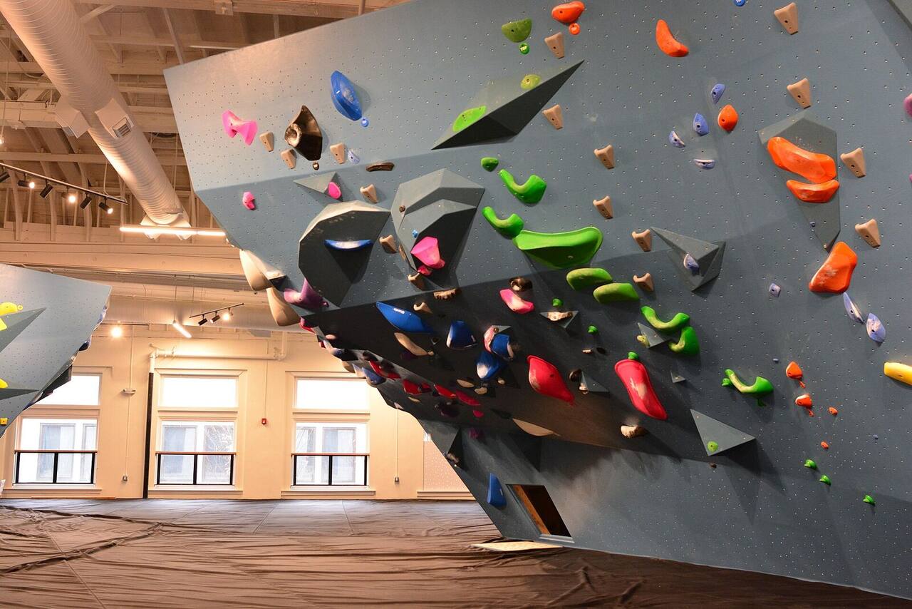 A steep grey bouldering overhang covered in fresh holds, tall windows behind